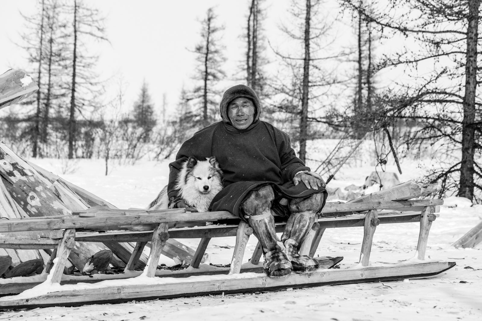 Fotografía en blanco y negro de esquimal en tundra, sentado en un trineo.